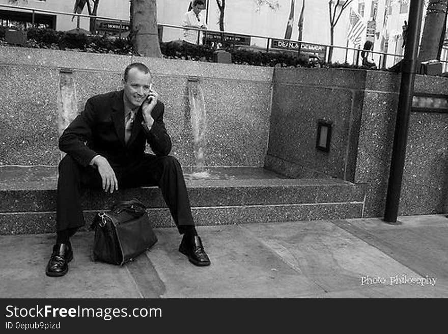 Businessman sitting on sidewalk outside using cellphone in black and white. Businessman sitting on sidewalk outside using cellphone in black and white.