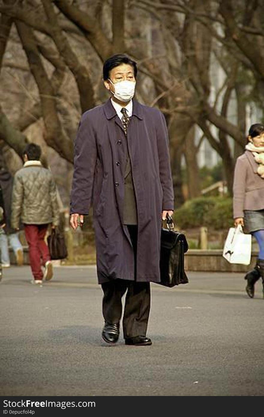 Asian businessman wearing white surgical face mask walking streets on sunny day. Asian businessman wearing white surgical face mask walking streets on sunny day.