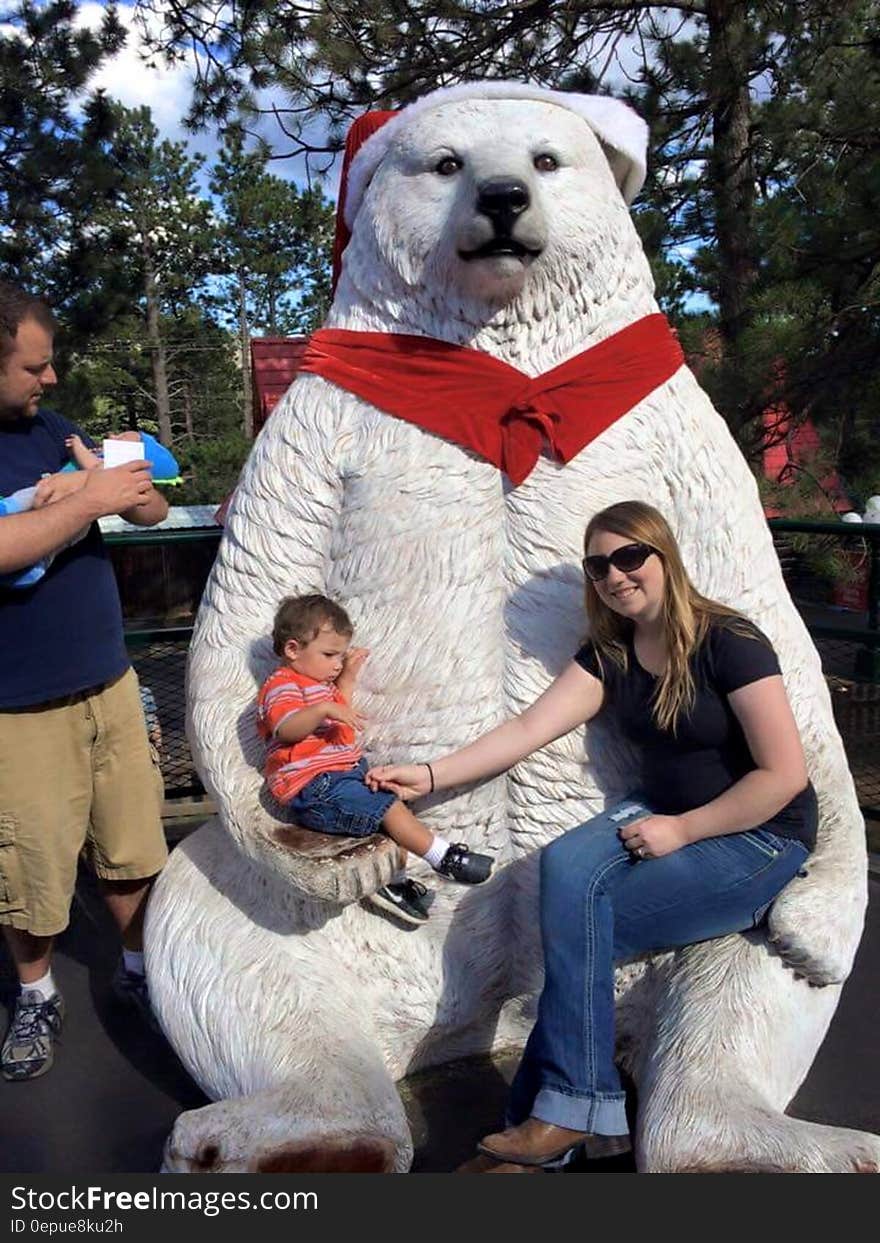 Family posing in front of white polar bear statue with red scarf and Christmas Santa hat on sunny day. Family posing in front of white polar bear statue with red scarf and Christmas Santa hat on sunny day.