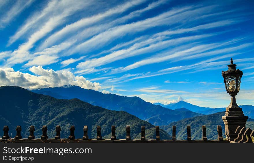 Dramatic white clouds in blue skies over mountain range above metal fencing and lamppost. Dramatic white clouds in blue skies over mountain range above metal fencing and lamppost.