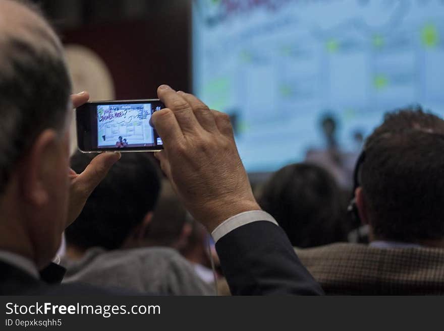 Man in business suit recording event from audience using smartphone. Man in business suit recording event from audience using smartphone.