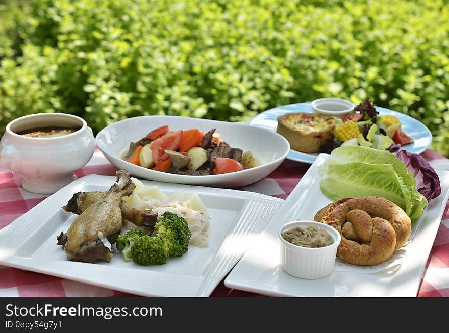 White china plates with food on table in sunny garden next to green bush. White china plates with food on table in sunny garden next to green bush.