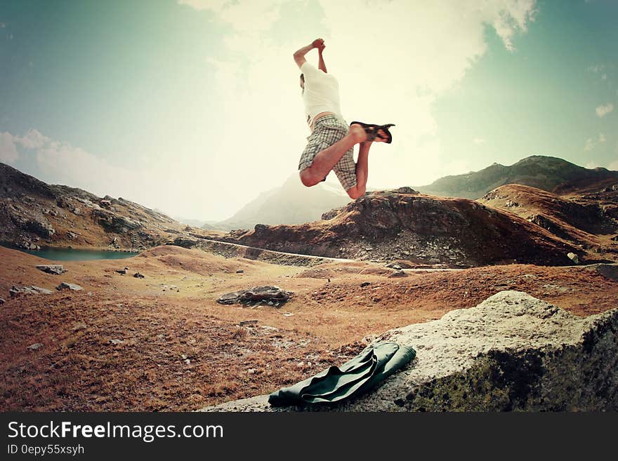 Man jumping in mountains along alpine lake on sunny day.