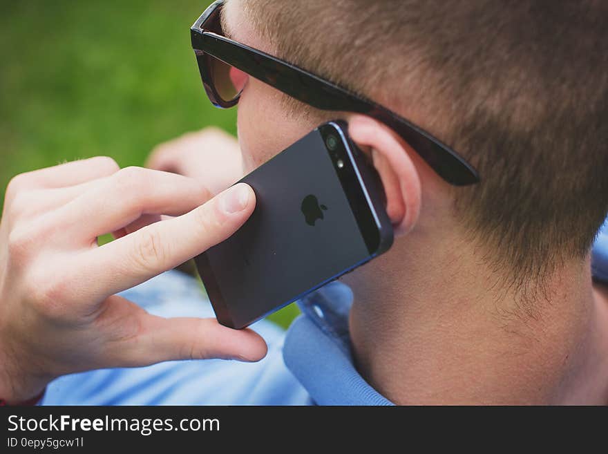 Man wearing sunglasses and blue shirt using cellphone outdoors. Man wearing sunglasses and blue shirt using cellphone outdoors.