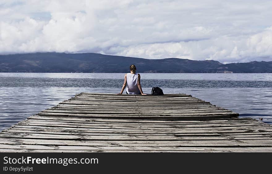 Person Sitting on Brown Wooden Dock Under Cloudy Blue Sky