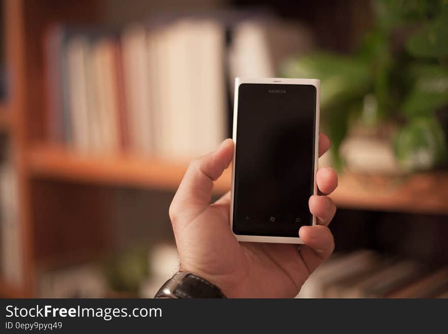 Person holding a smartphone with book shelves in background.