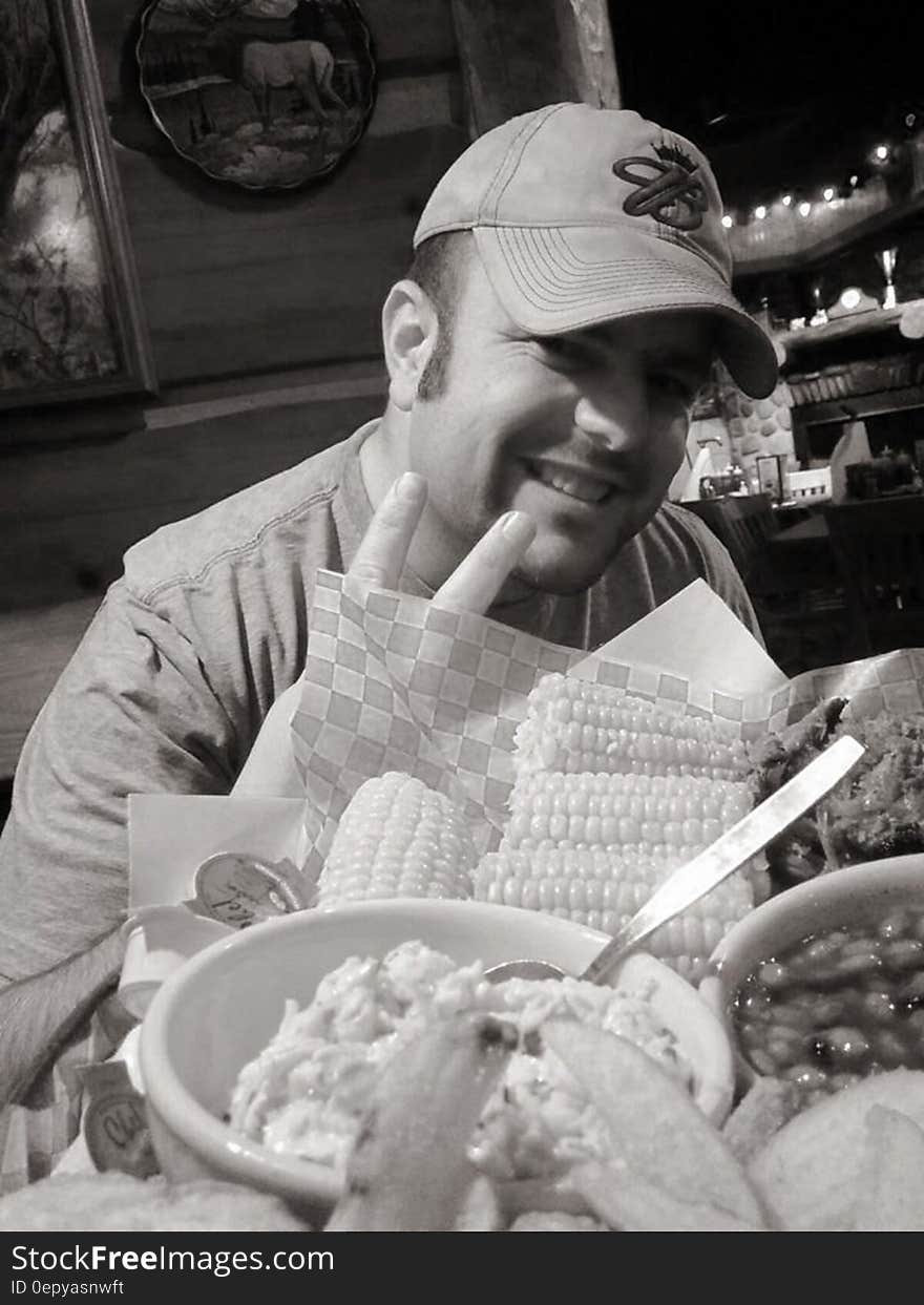 Man in ball cap smiling and gesturing white eating at restaurant in black and white. Man in ball cap smiling and gesturing white eating at restaurant in black and white.