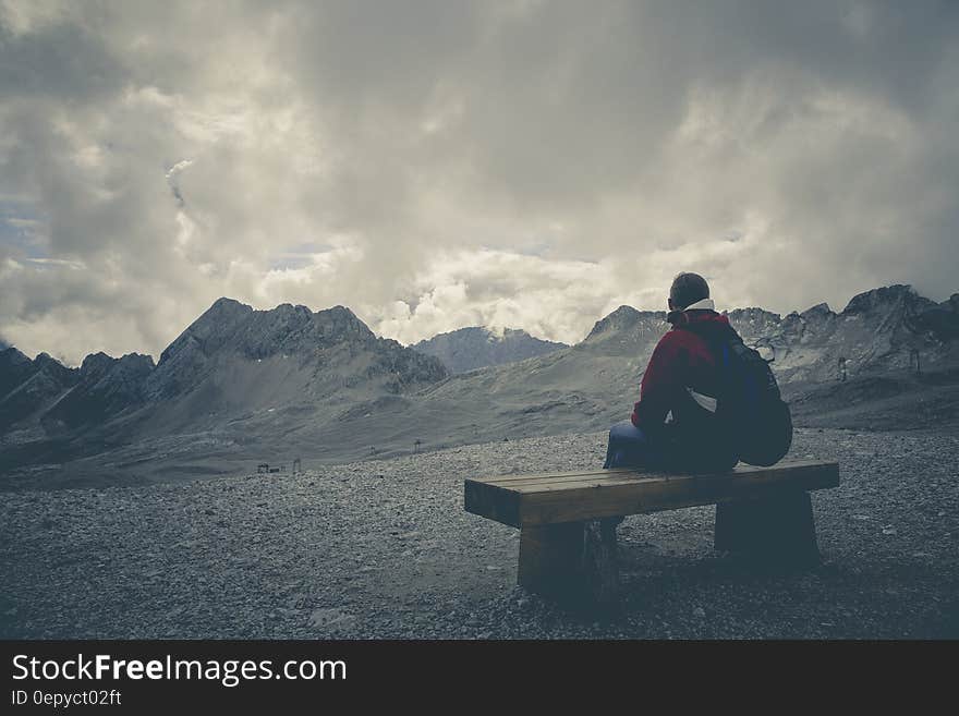 Man in Red Jacket Sitting on Brown Wooden Bench