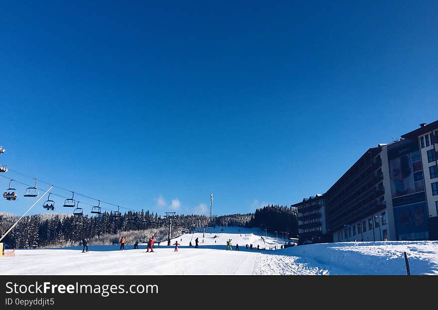 People on a Snowy Ski Hill With a Lift on the Left and a Hotel on the Right