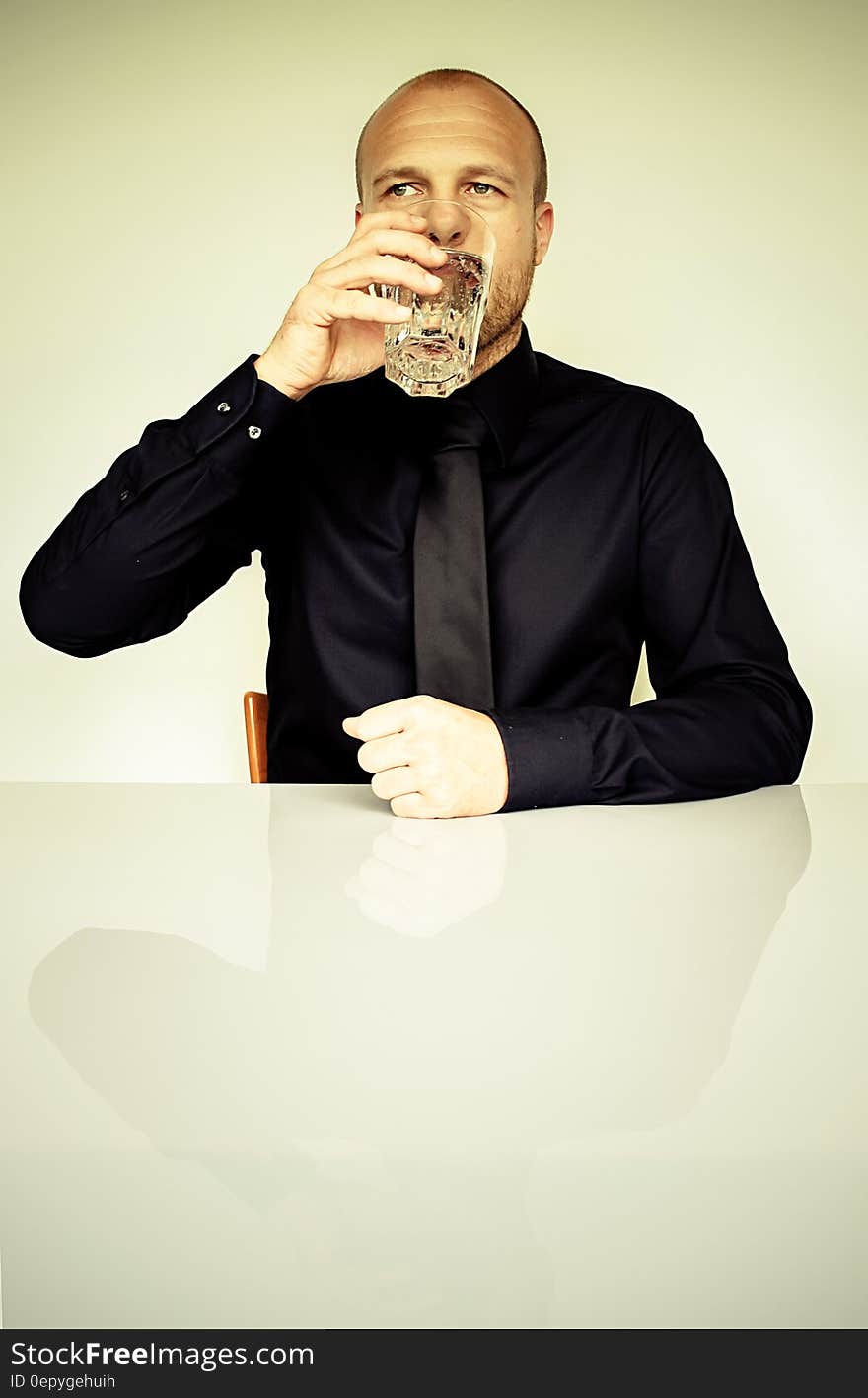 Man in Black Dress Shirt Sitting in Front of White Table Drinking Water