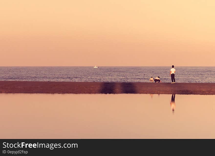 Man Standing Near Seashore With Boat in Distance Under Cloudy Sky during Daytime