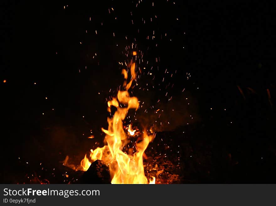 A burning bonfire with yellow flames and hot burning embers rising against a black sky. A burning bonfire with yellow flames and hot burning embers rising against a black sky.