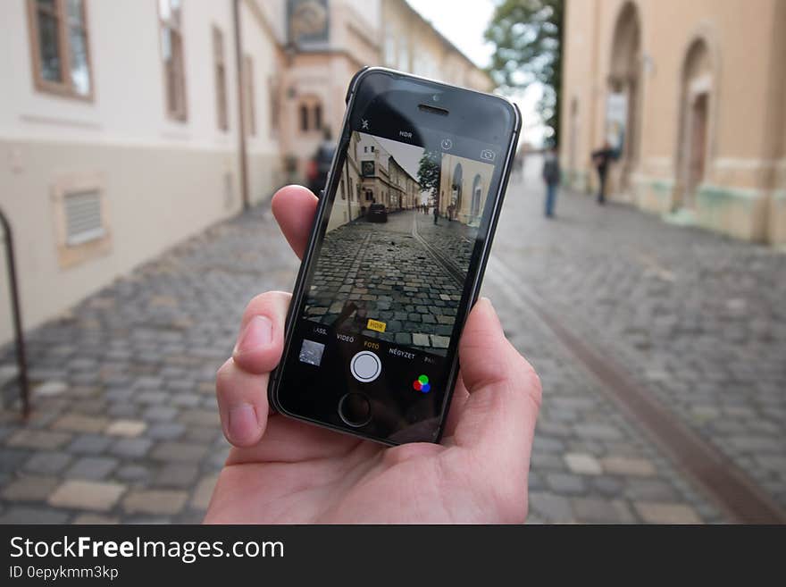 Person Taking a Photo of Empty Black and Gray Concrete Road Between Beige Paint Wall Concrete Building