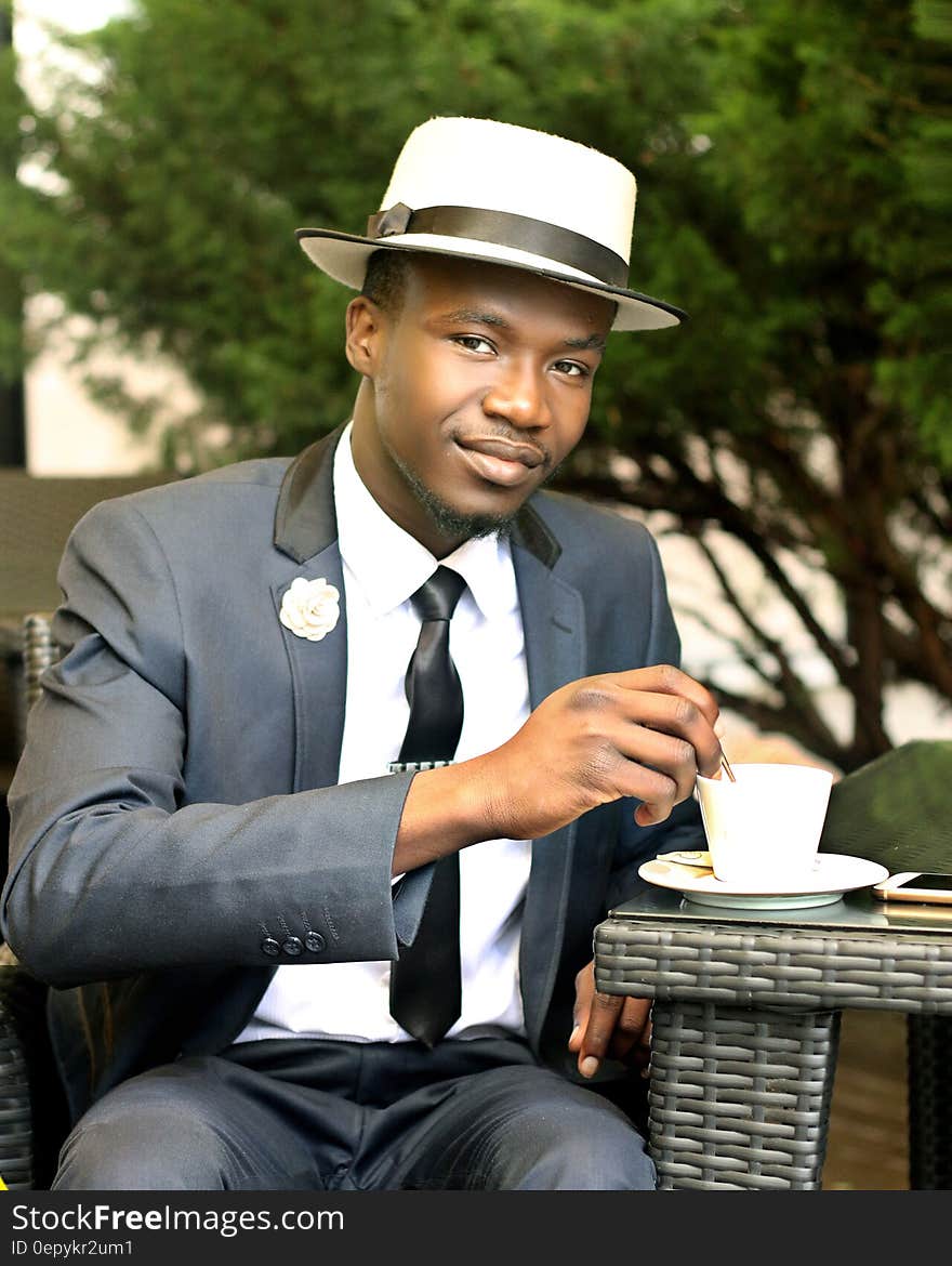 Man in Gray Formal Suit Jacket Stirring Coffee during Daytime