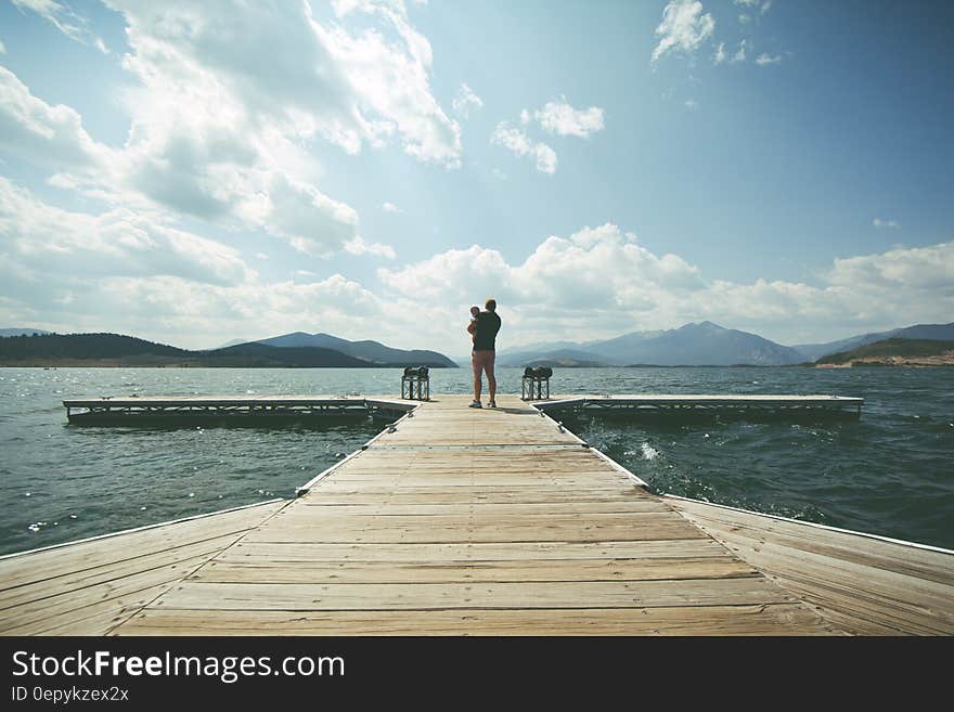 Person Standing on Brown Wooden Dock Under Clue Sky during Daytime