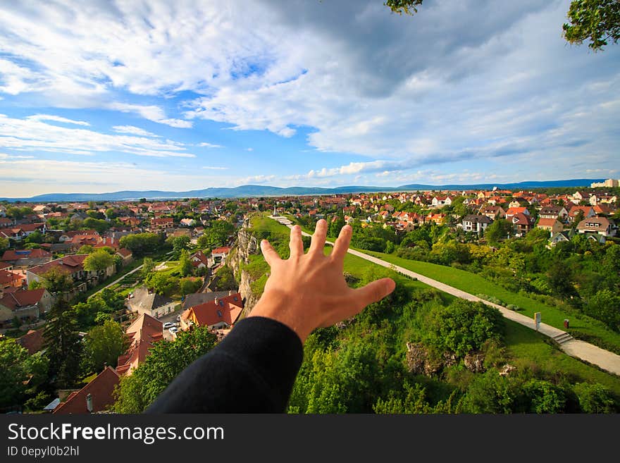 Human Hand Under White and Blue Sky on Green Grass Field