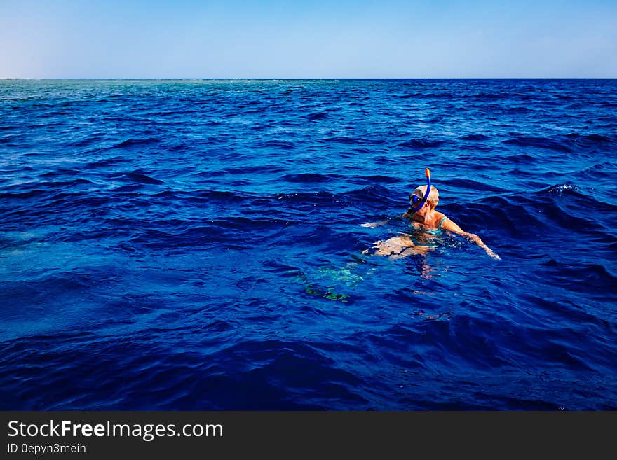 Snorkeler in blue waters with mask and breathing tube on sunny day.