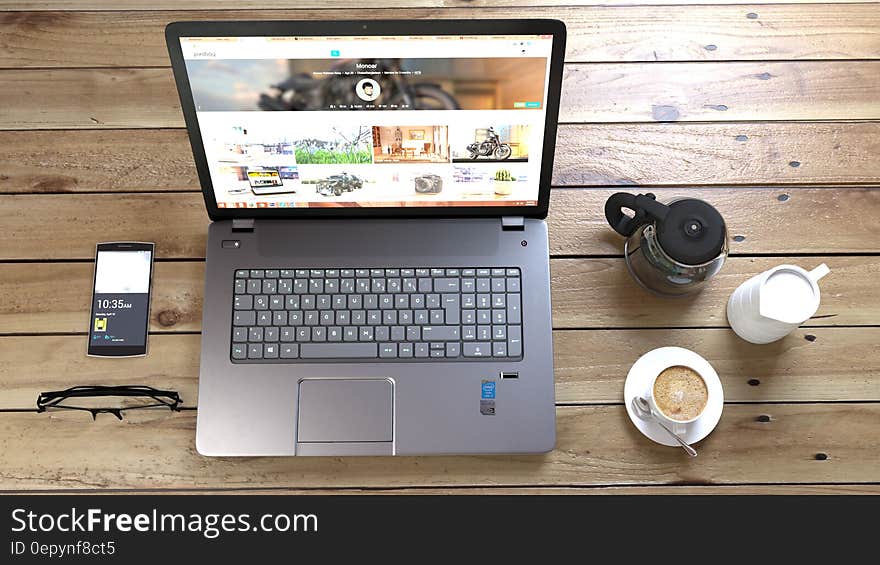 Silver Laptop Next to Coffe Cup Smartphone and Glasses