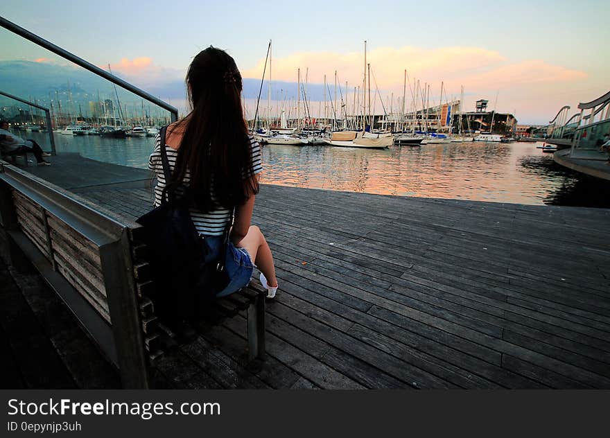 Woman in Black and White Stripe Scoop Neck Shirt Sitting on Brown Wooden Bench in Ship Dock during Daytime