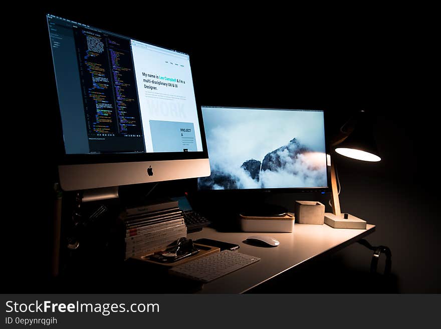 Apple computer screens on desk in dark room. Apple computer screens on desk in dark room.