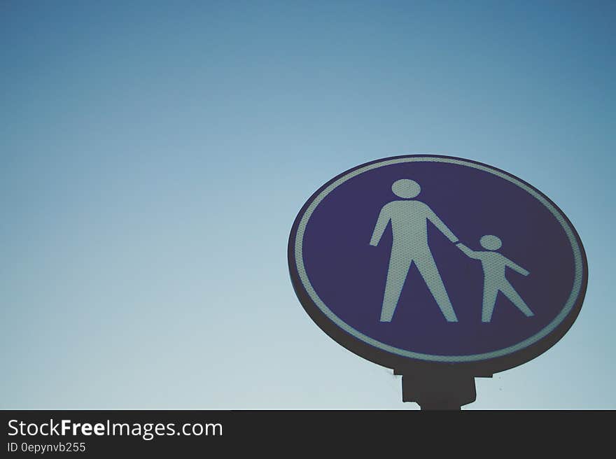 Blue and white sign with adult and child against blue skies on sunny day. Blue and white sign with adult and child against blue skies on sunny day.