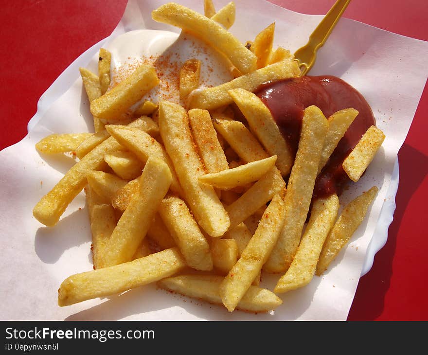 Basket of french fries and catsup on red table.