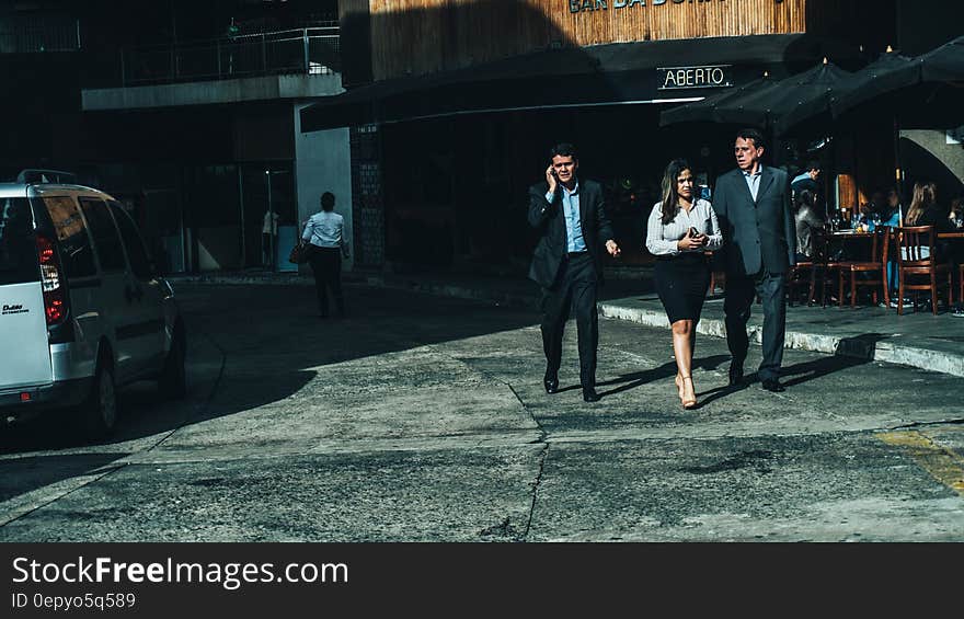 Woman in White Dress Shirt Between Men in Suit Standing on Concrete Ground