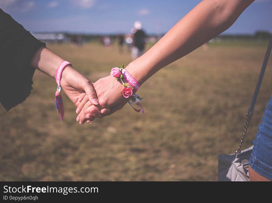 2 Person Holding Each Other Wearing Pink Friendship Bracelet during Daytime