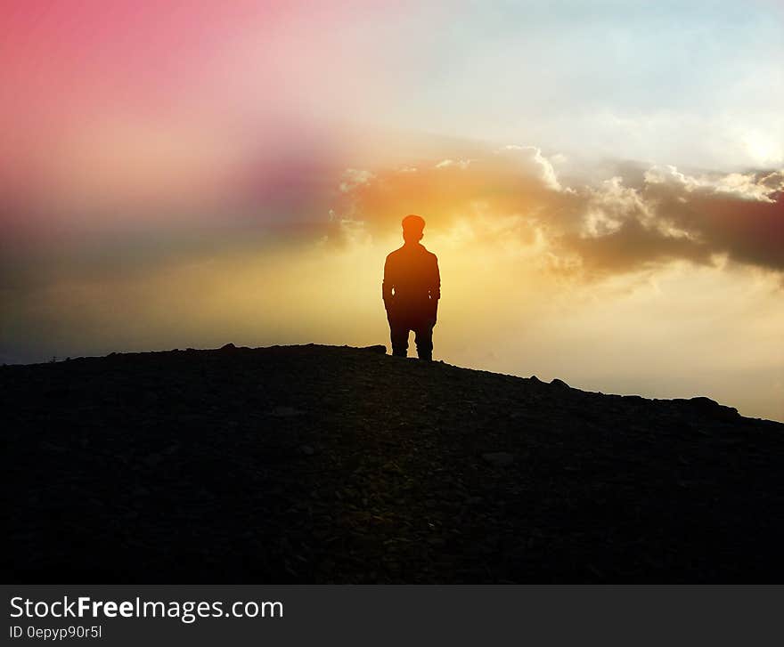 A silhouette of a man standing on a hilltop at sunset. A silhouette of a man standing on a hilltop at sunset.