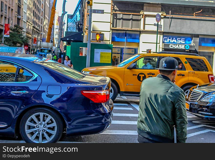 Pedestrian waiting on sidewalk with traffic through busy crosswalk intersection on sunny day. Pedestrian waiting on sidewalk with traffic through busy crosswalk intersection on sunny day.