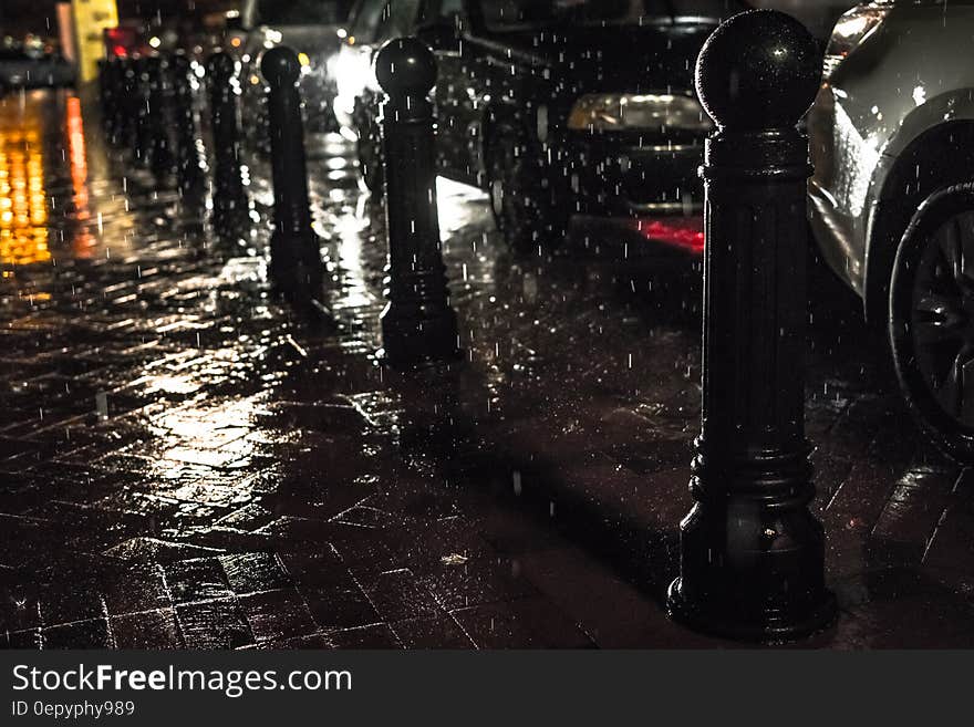 Black Posts on Black Pavement Beneath Falling Rain