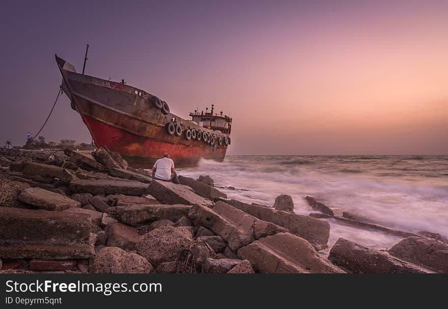 Red Blue and Black Photo of a Ship and a Man Sitting on a Stone Near Seashore