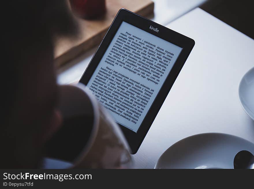 Person reading book on Amazon Kindle reader and drinking coffee.