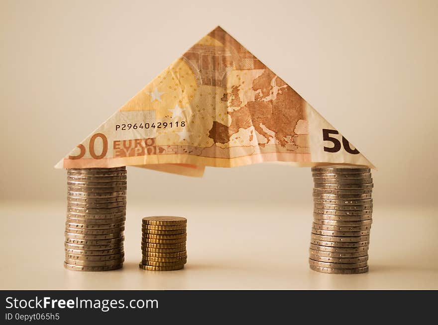 Euro note folded into triangle balanced on stack of coins. Euro note folded into triangle balanced on stack of coins.