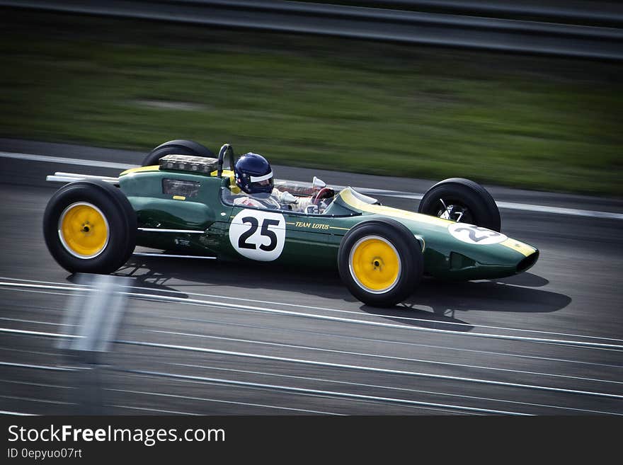 Formula 0ne green racing car numbered 25 traveling at speed on race circuit with white lane markings and green grassy background. Formula 0ne green racing car numbered 25 traveling at speed on race circuit with white lane markings and green grassy background.