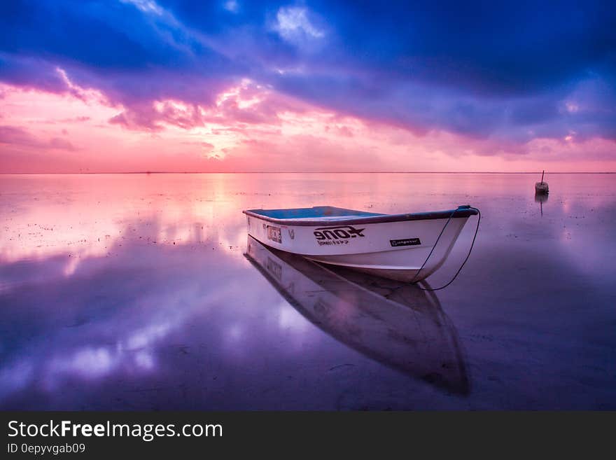 Wooden boat in clear waters reflecting clouds and colors at sunset. Wooden boat in clear waters reflecting clouds and colors at sunset.