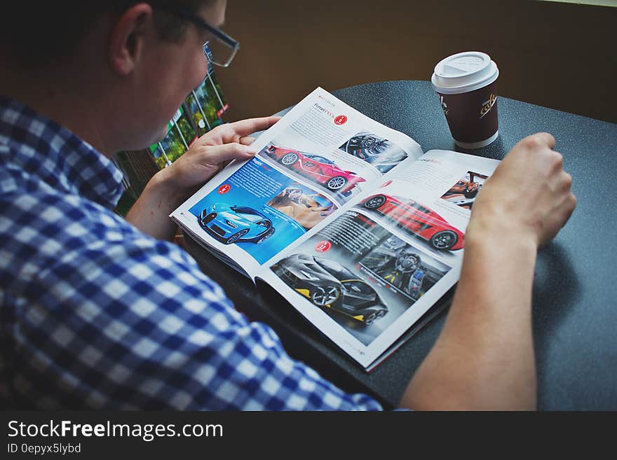 Man in Blue and White Gingham Print Shirt Reading Car Magazine