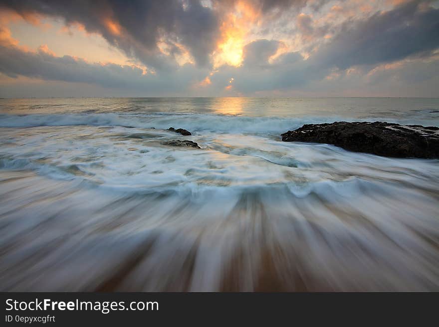 Time Lapse Photo of Water Current and Brown Rock Under White and Yellow Cloudy Sky