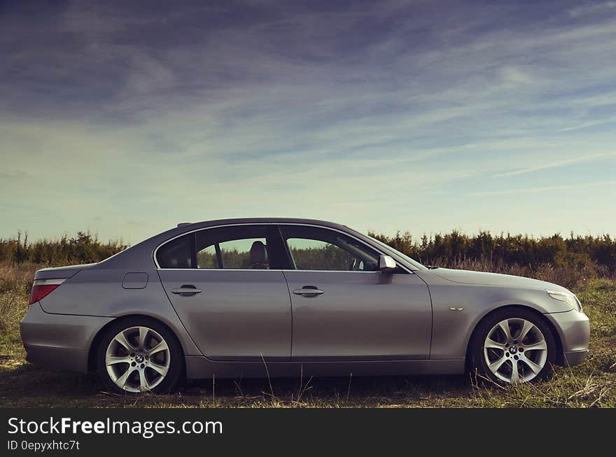 Silver Sedan Parked Far from Green Trees Under Blue Sky during Daytime