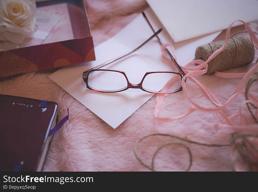 Eyeglasses Beside Pink Yarn on Pink Bed Blanket