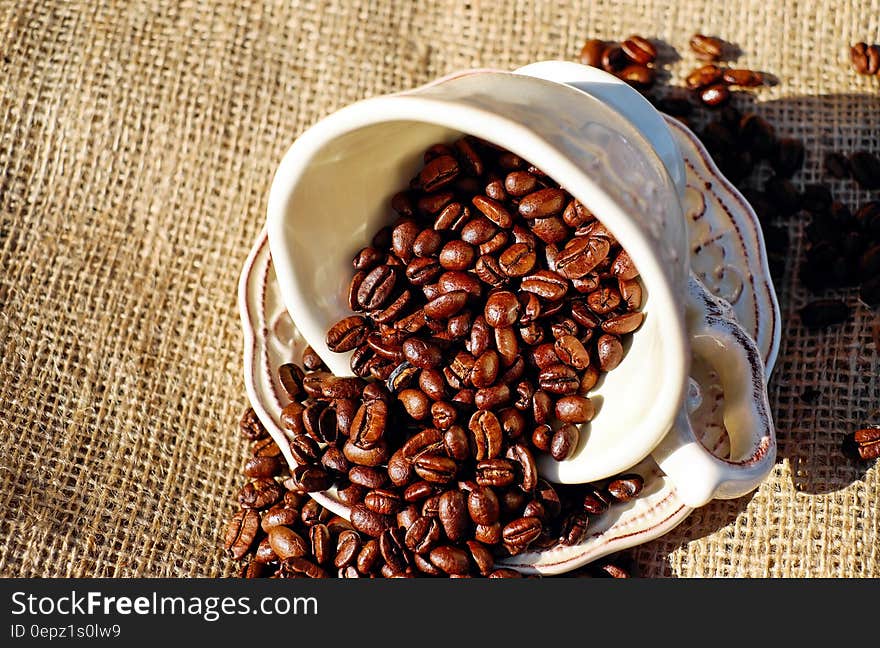 Close up of white china cup and saucer with roasted coffee beans on burlap. Close up of white china cup and saucer with roasted coffee beans on burlap.