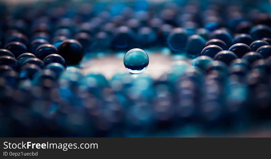 This picture shows a large number of blue opaque glass marbles. In the middle there is a round free space around a single marble located exactly in the center of the picture. This picture shows a large number of blue opaque glass marbles. In the middle there is a round free space around a single marble located exactly in the center of the picture.