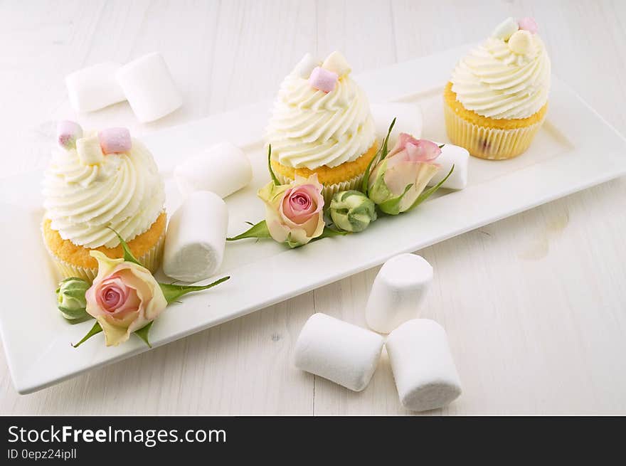 Marshmallows next to tray of frosted cupcakes with rose buds. Marshmallows next to tray of frosted cupcakes with rose buds.