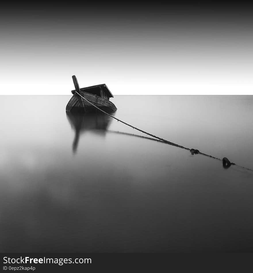 A black and white photo of an anchored wooden boat on still sea surface. A black and white photo of an anchored wooden boat on still sea surface.