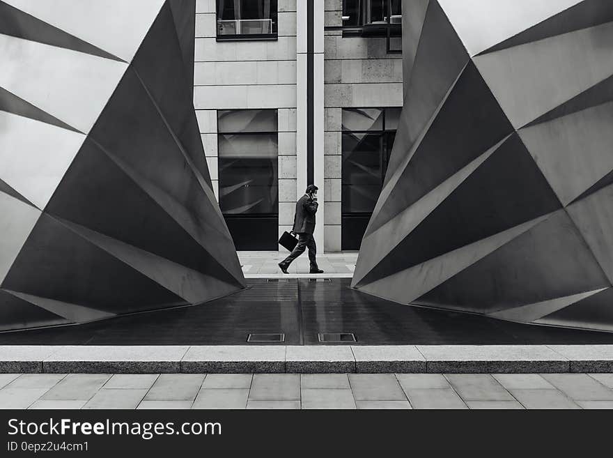 A monochrome photo of a businessman in a hurry, carrying a briefcase, walking past a modern building. A monochrome photo of a businessman in a hurry, carrying a briefcase, walking past a modern building.