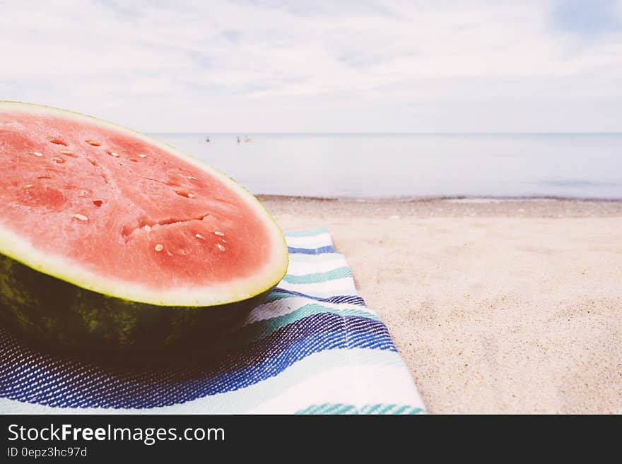 Slice of watermelon on beach blanket on sandy shores.