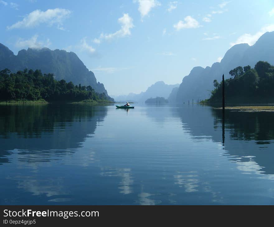 Kayak on blue waters reflecting mountain landscape on sunny day.