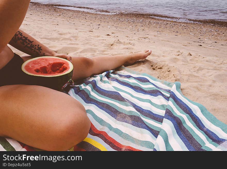 A woman eating a watermelon white sitting on the beach. A woman eating a watermelon white sitting on the beach.