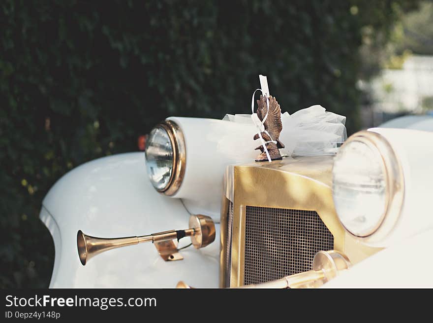 Headlights and hood ornament on front of white vintage car outdoors on sunny day. Headlights and hood ornament on front of white vintage car outdoors on sunny day.