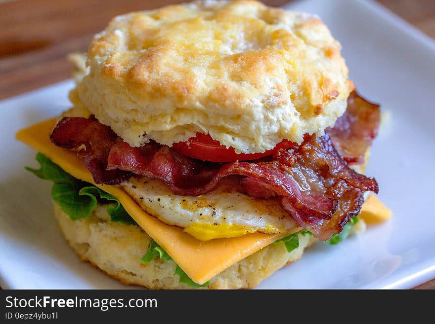 Close up of biscuit sandwich with bacon, egg, cheese and lettuce on white plate. Close up of biscuit sandwich with bacon, egg, cheese and lettuce on white plate.